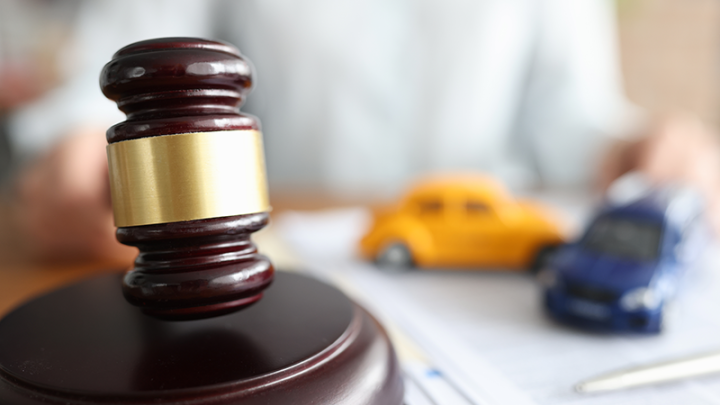 A closeup of a gavel with two model cars in the background. 
