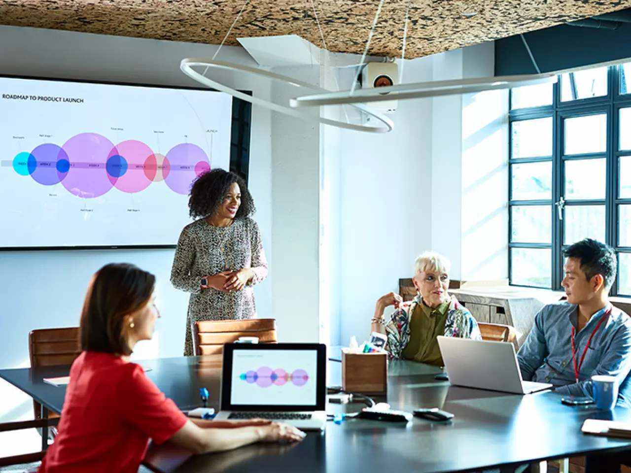 A group of colleagues around a conference table with a presentation playing in the background