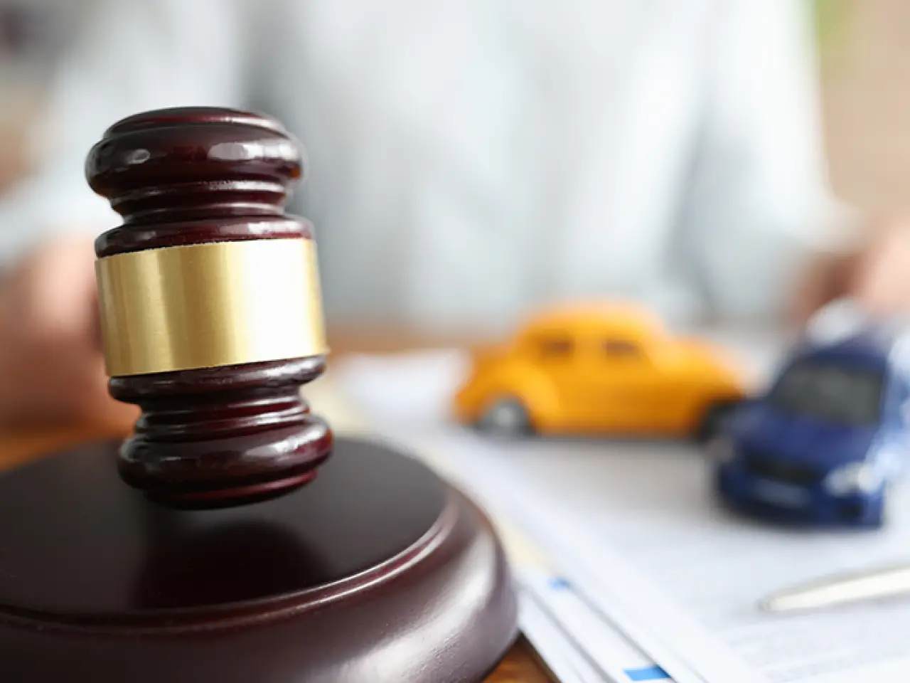 A closeup of a gavel with two model cars in the background.