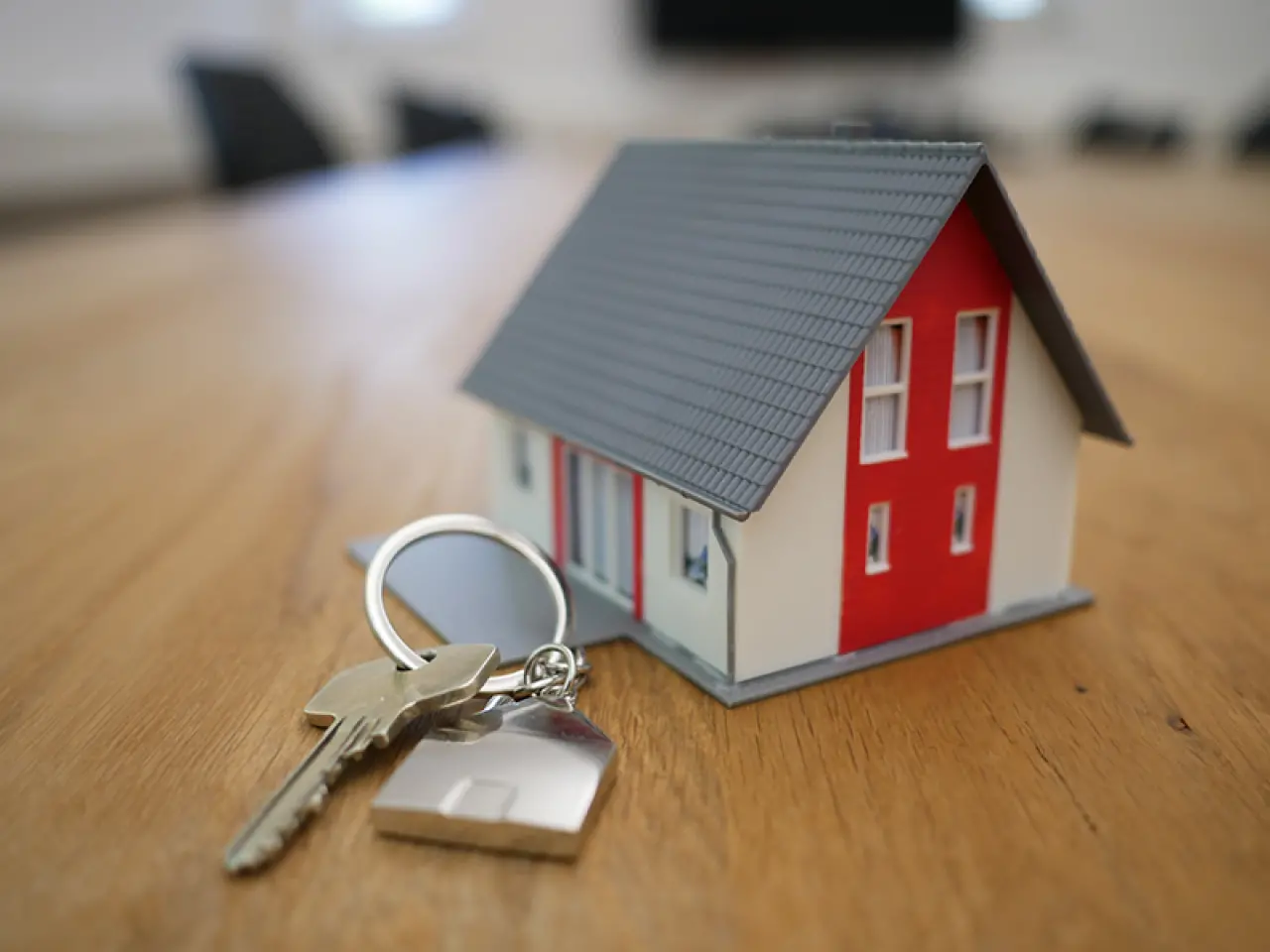 A close-up of a set of house keys next to a miniature house.