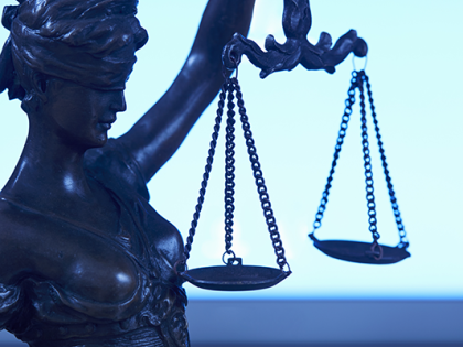 A statue of Lady Justice holding her scales in front of a laptop. 