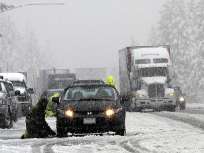 Cars and trucks driving and stuck on a slushy icy road as snow falls. 