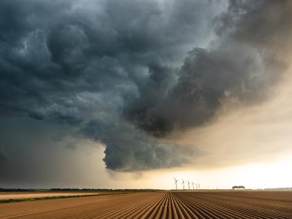 A landscape of flat farm fields. Threatening dark clouds indicating a storm is brewing sit blocking out the sunlight.